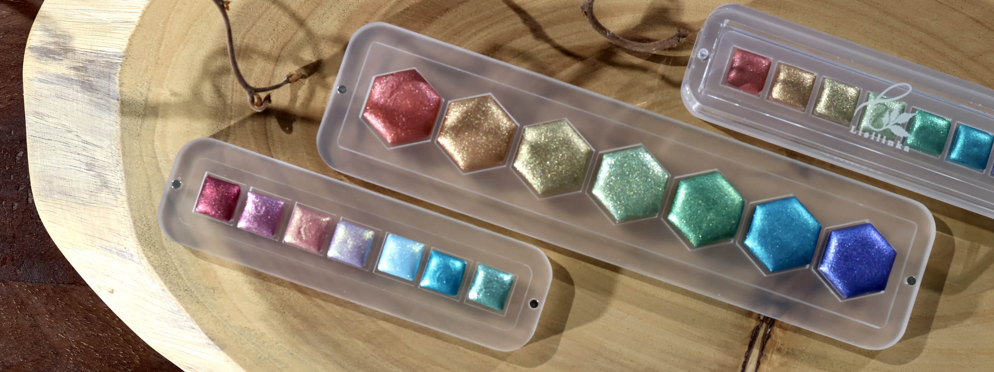 Lisilinka Opal set with six iridescent metallic watercolors in rainbow colors displayed in clear acrylic storage box on wooden surface together with the upcoming May Giveaway 2026